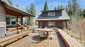 Eine Holzterrasse mit Sitzgelegenheiten im Freien, eine überdachte Terrasse und ein Haus mit großen Fenstern und einem geneigten Dach.