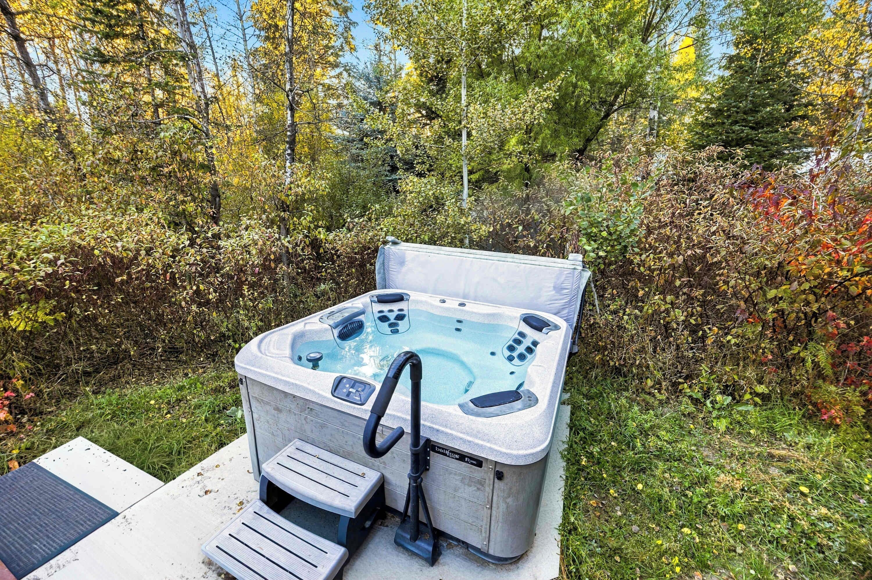 Un jacuzzi con panel de control y manguera, sobre una superficie de concreto con un banco de madera cercano.