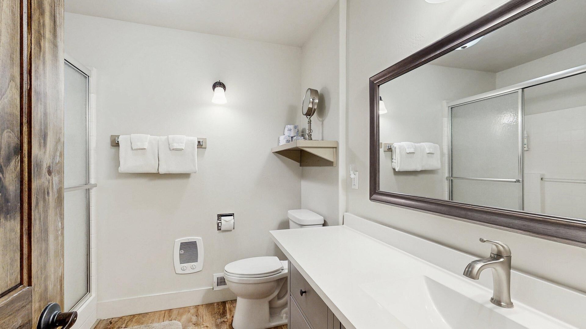 A bathroom with a toilet, sink, mirror, towel rack, and a vent.