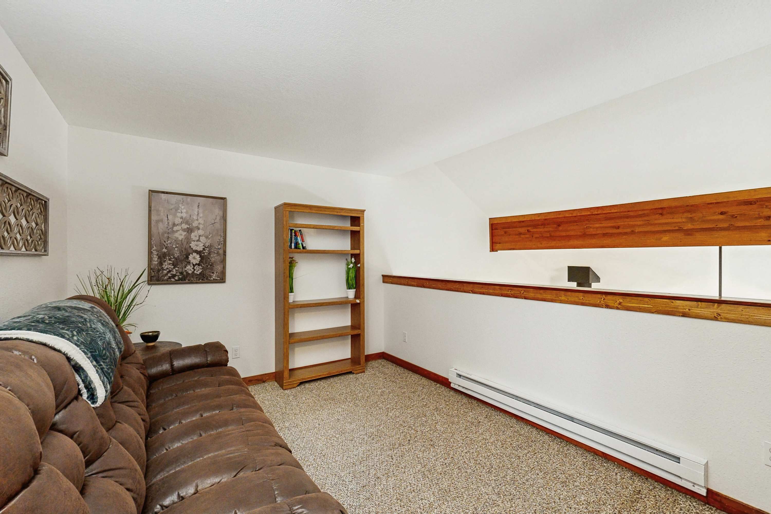 A living room with a brown leather sofa, a wooden bookshelf, a framed picture, and a white radiator.