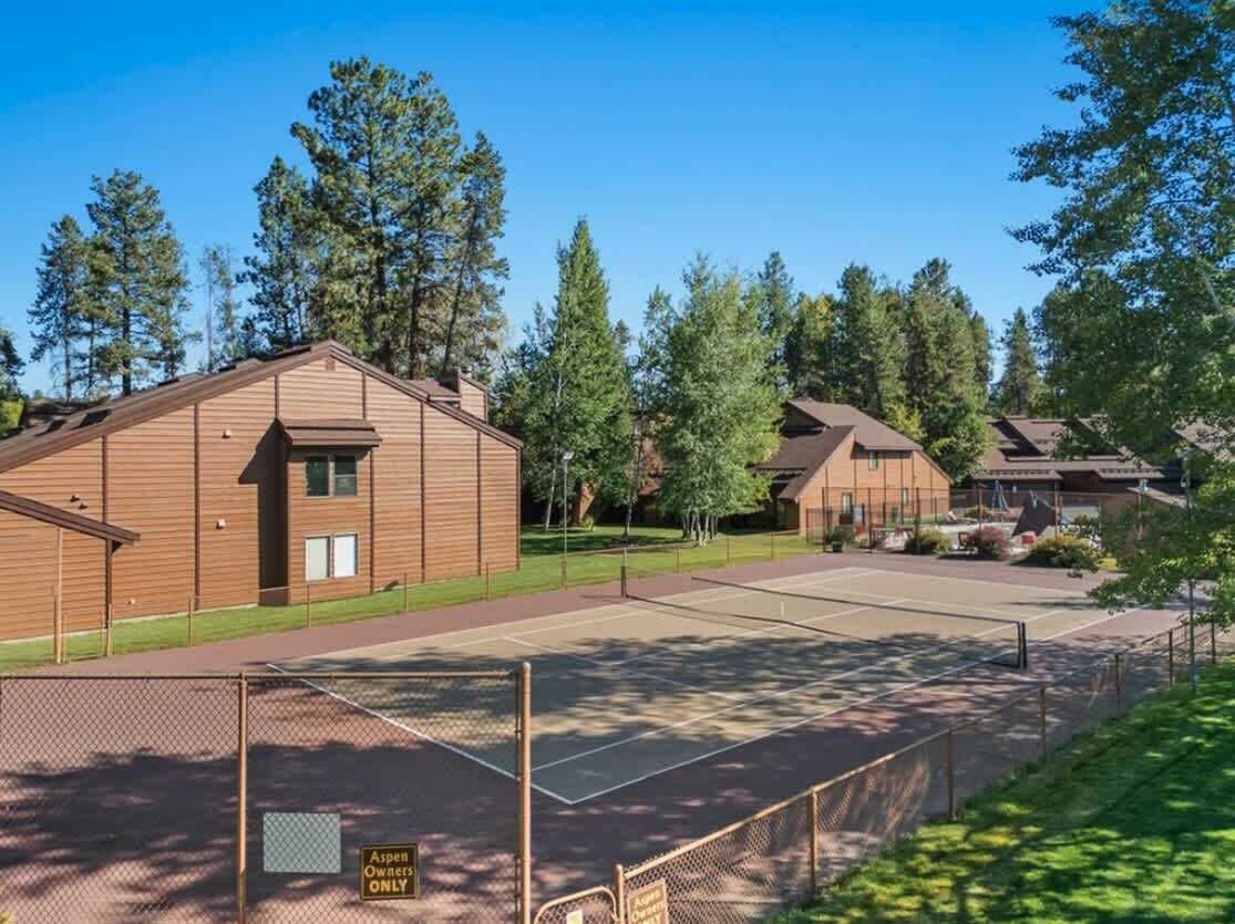 Un quartier résidentiel comprenant plusieurs maisons, un court de tennis clôturé et un panneau indiquant : « Réservé aux propriétaires d’Aspen ».