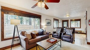 A spacious living room with a large window, a ceiling fan, and a fireplace. - Downtown McCall Retreat | Wood Stove & Deck (McCall)