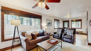 A spacious living room with a large window, a ceiling fan, and a fireplace.