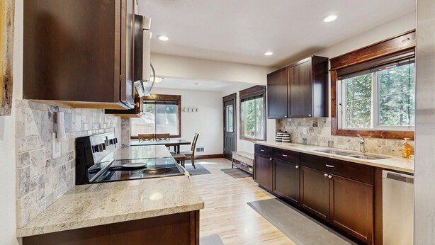 A modern kitchen with dark wood cabinets, a granite countertop, and a large window providing a view of the outdoors. - Downtown McCall Retreat | Wood Stove & Deck (McCall)