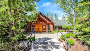 A log cabin with a large wooden door, a stone chimney, and a concrete staircase leading to the entrance.