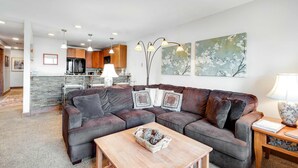 A modern living room with a sectional sofa, a wooden coffee table, and a kitchen in the background. - McCall Condo | Walk to Lake, Shops & Parks (McCall)