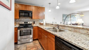A modern kitchen with wooden cabinets, stainless steel appliances, granite countertops, and pendant lighting. - McCall Condo | Walk to Lake, Shops & Parks (McCall)