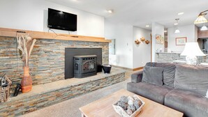 A modern living room with a stone fireplace, a flat-screen TV, and a grey sofa. - McCall Condo | Walk to Lake, Shops & Parks (McCall)