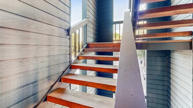 A wooden staircase with a metal handrail, leading to an upper level. - Downtown McCall Condo | Fireplace + Balcony (McCall)