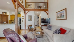 A spacious living area with a high wooden ceiling, a kitchen with wooden cabinets, a dining area, and a TV mounted on the wall. - Golf Course Retreat | Patio & Near Downtown McCall (McCall)