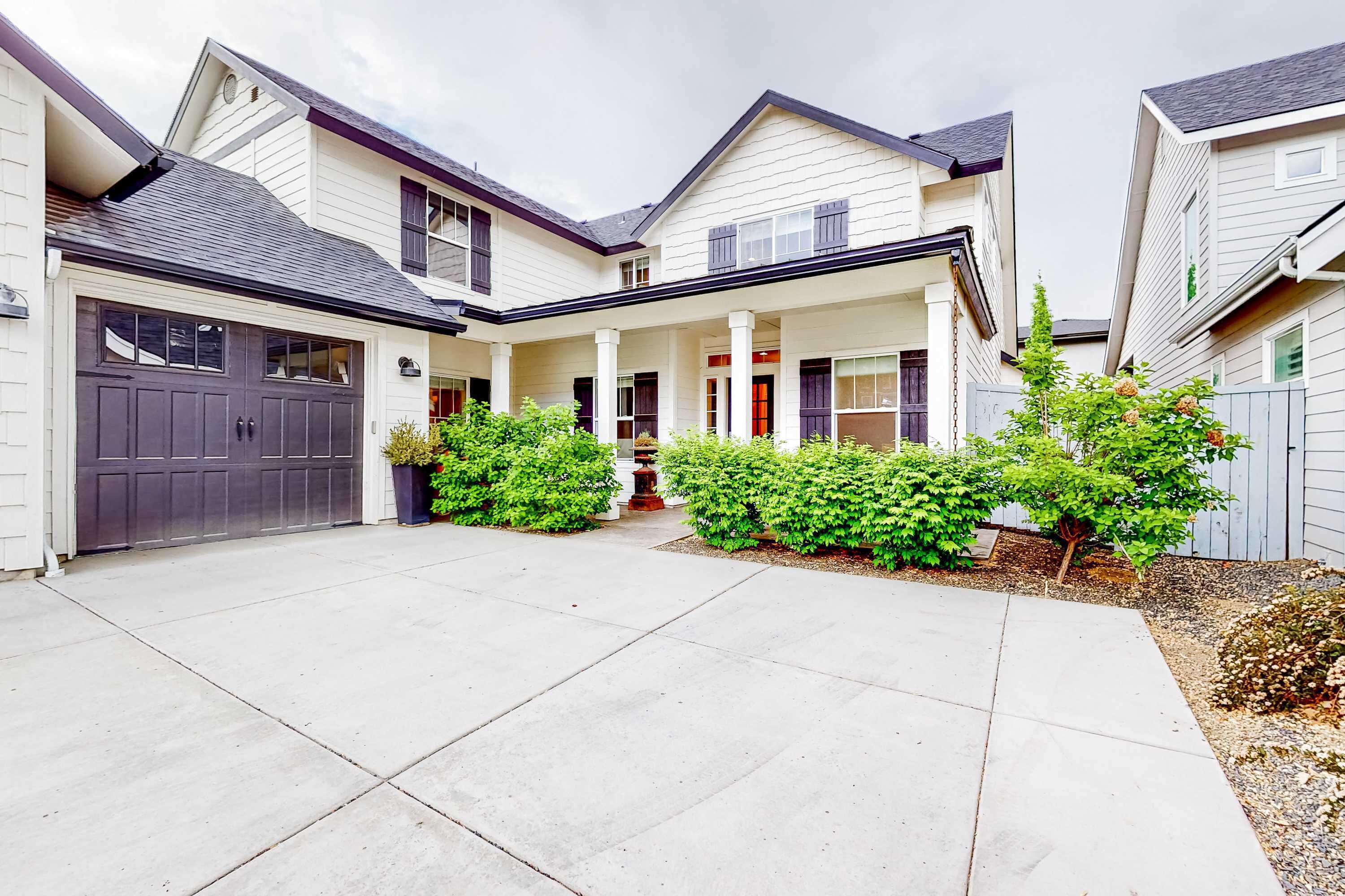 A two-story house with a covered front porch, a garage, and a well-maintained front yard with shrubs and a small tree.