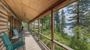 Eine überdachte Terrasse mit Holzgeländern, Stühlen und Blick auf einen von Bäumen umgebenen See.