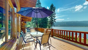 A wooden deck with a table and chairs, a purple umbrella, and a view of a lake and mountains.