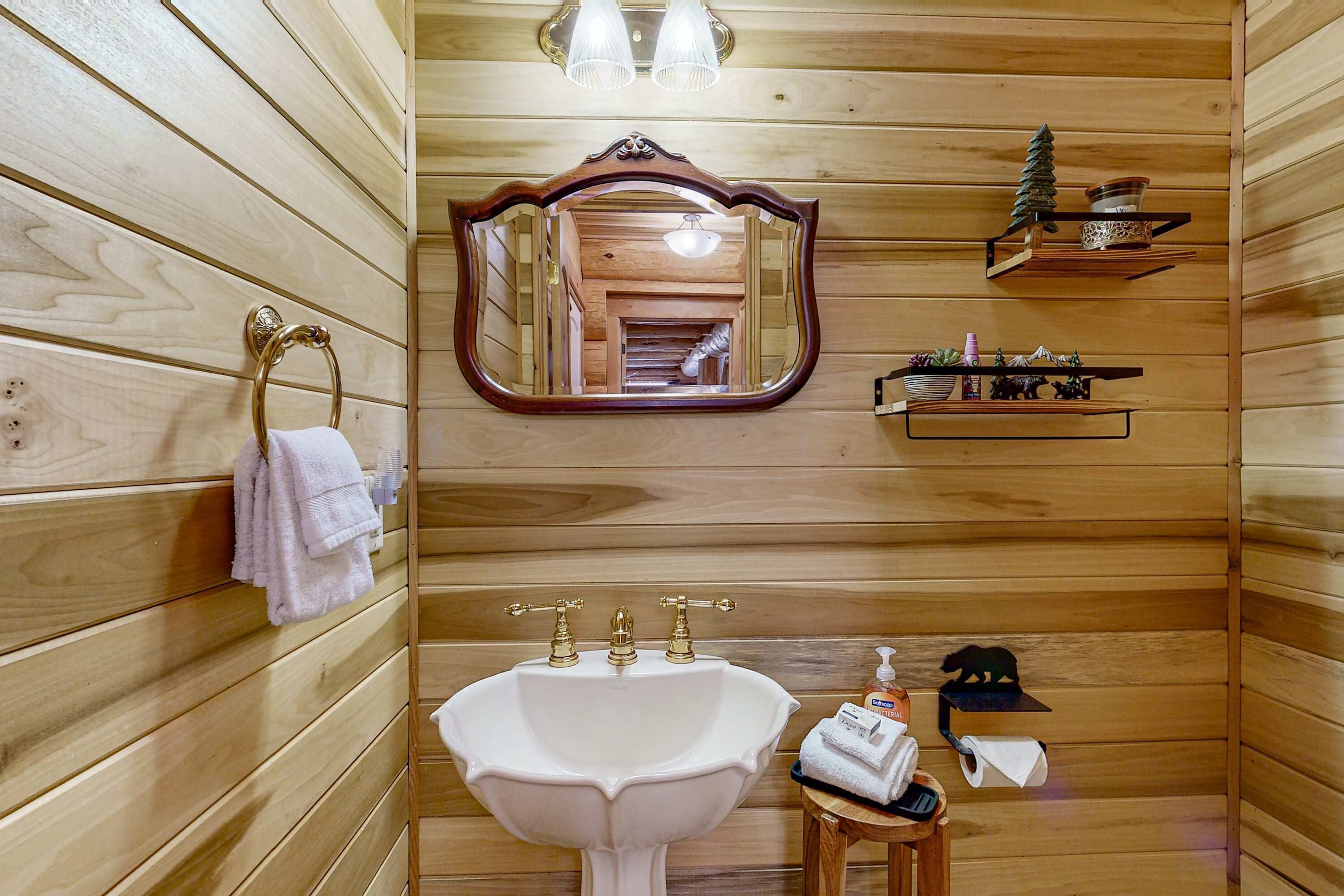 Un baño de cabaña de madera con un lavamanos blanco, un espejo y un perchero para toallas.