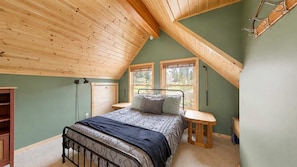 A bedroom with a sloped ceiling, a bed, a bedside table, a chair, and a window.