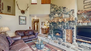 A living room with a stone fireplace, leather sofas, a glass coffee table, and a television.