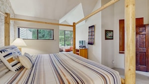 A bedroom with a large bed, a window, a television, and a wooden door.