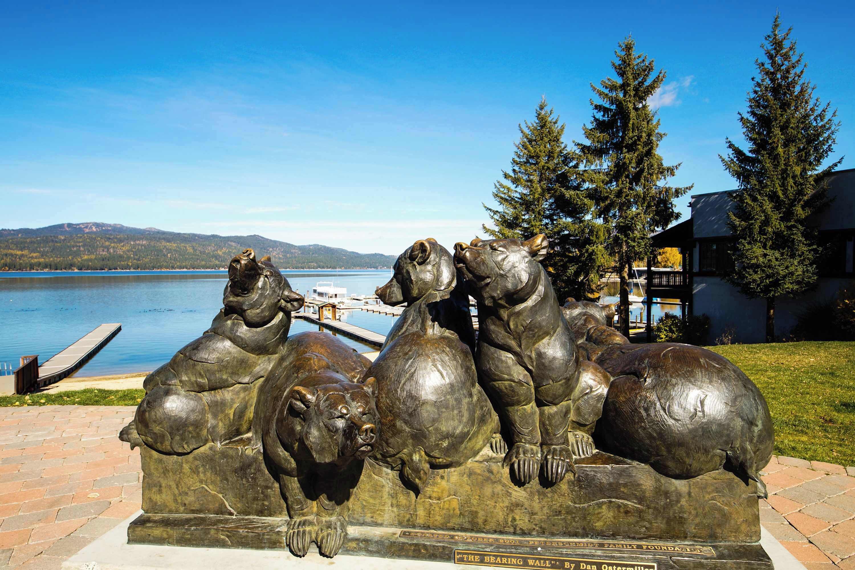 En bronzeskulptur af bjørne på en bænk ved en sø.