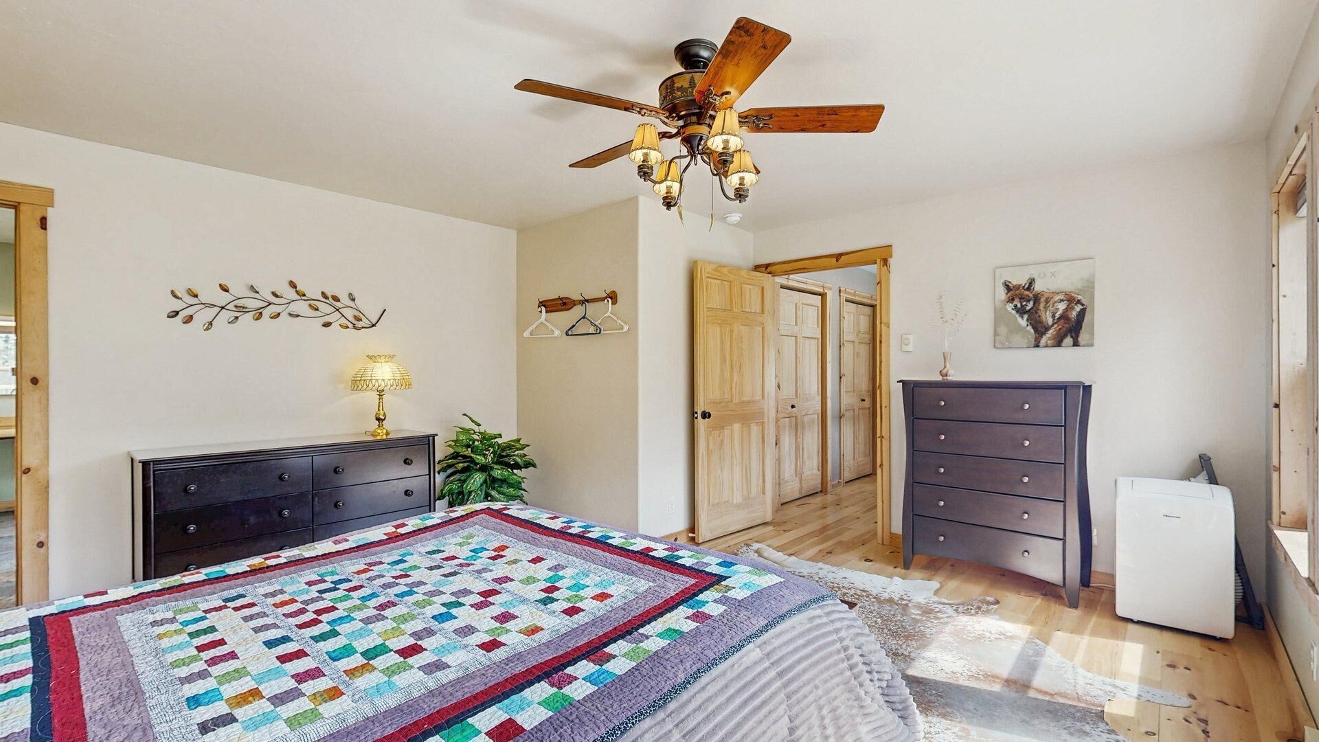 Ein Schlafzimmer mit einem Bett, einem Schminktisch, einem Schreibtisch, einem Deckenventilator und einer Tür zu einem anderen Raum.