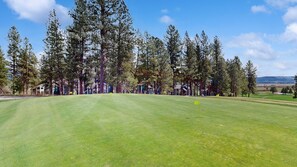 A golf course with a well-maintained green, tall trees, and distant houses. - New Meadows Retreat | Large Deck, Fire Pit, Resort (New Meadows)