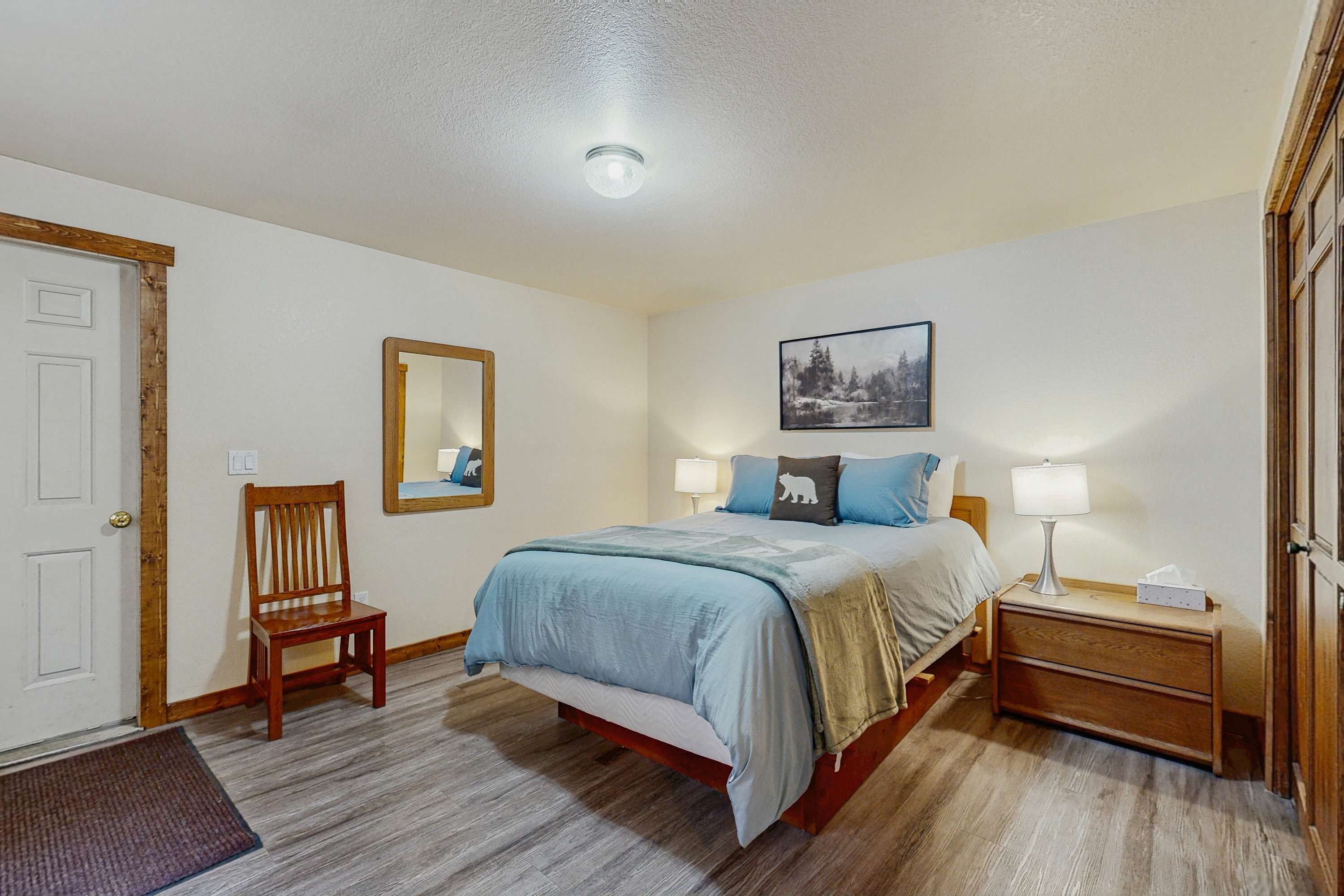 Een slaapkamer met een bed, nachtkastje, stoel en een deur.