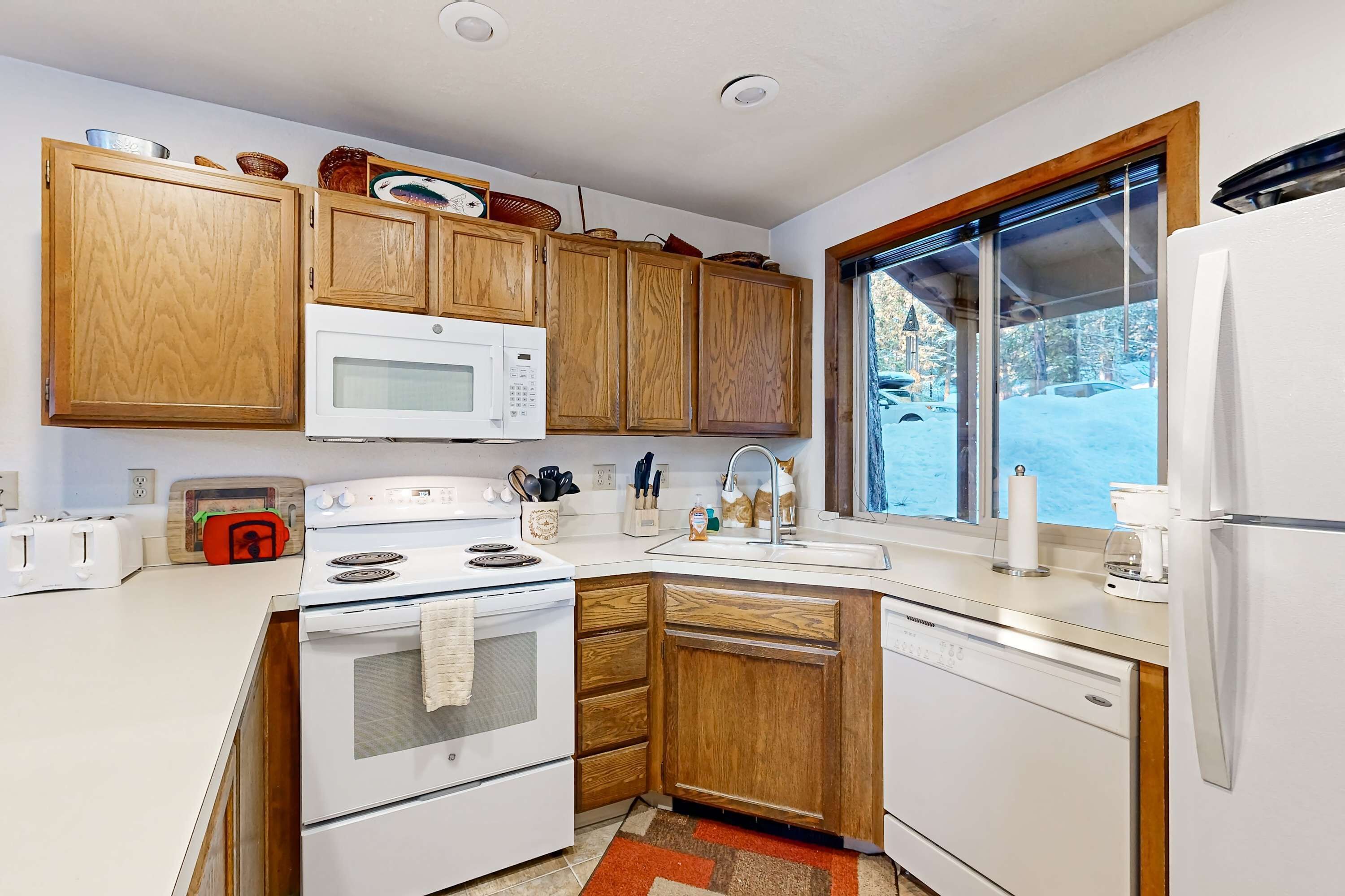 A modern kitchen with wooden cabinets, white appliances, and a large window.