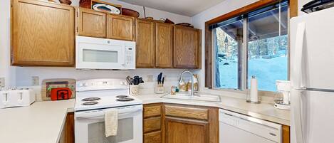 A modern kitchen with wooden cabinets, white appliances, and a large window.