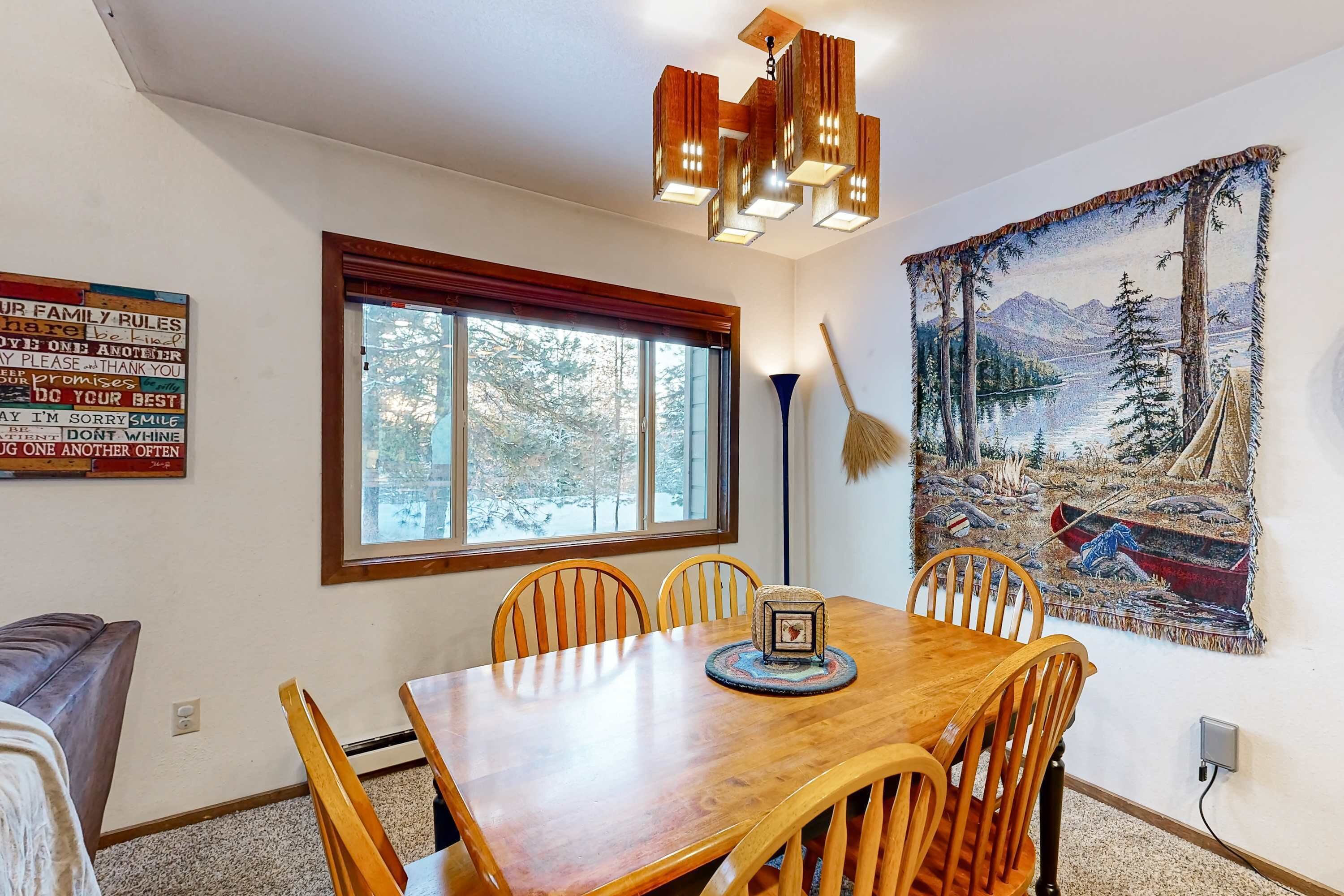 A dining area with a wooden table, chairs, a chandelier, a window, and a tapestry on the wall.