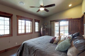 Une chambre avec un grand lit, des fenêtres en bois, un ventilateur de plafond et une armoire intégrée.