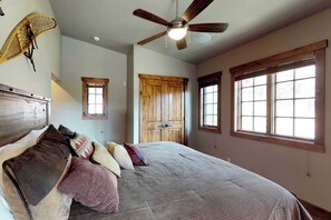 A bedroom with a large bed, a ceiling fan, a wooden door, and two windows. - Tamarack Ski-In/Out Cottage, Fire Pit, Sleeps 6 (Donnelly)