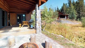 Una cabaña de madera con un pilar de piedra, terraza de madera y una fogata.