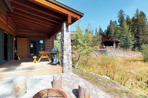 Une cabane en bois avec un pilier en pierre, une terrasse en bois et un foyer.