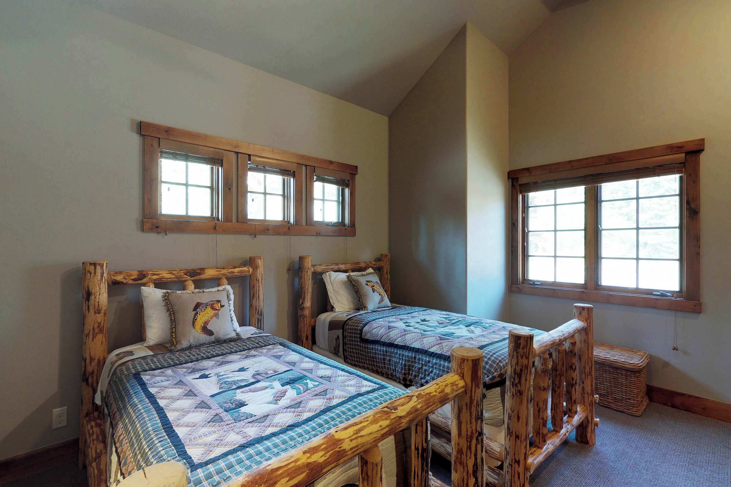 A room with two wooden beds, each with a quilt and pillows, and a window above each bed.
