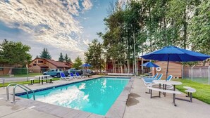 Ein Swimmingpool mit Liegestühlen und Sonnenschirmen, umgeben von Bäumen und einem Zaun.