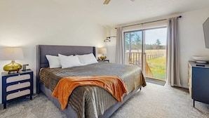 Makuuhuoneessa on suuri sänky, yöpöytä, lamppu, kattotuuletin, ikkuna, jossa on verhot, ja näkymä ulos.
