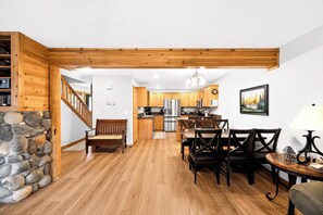 Un vaste espace de vie agrémenté d’un escalier en bois, d’une table à manger avec des chaises, d’une cuisine équipée d’appareils modernes et d’un mur d’accent en pierre.