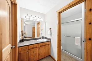 Une salle de bain avec un meuble-lavabo en bois, un évier, un miroir avec éclairage intégré et une porte de douche en verre.