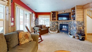 A cozy living room with a stone fireplace, wooden shelves, and a television. - 3BR Retreat | AC, Fireplace, Walk to Payette Lake (McCall)