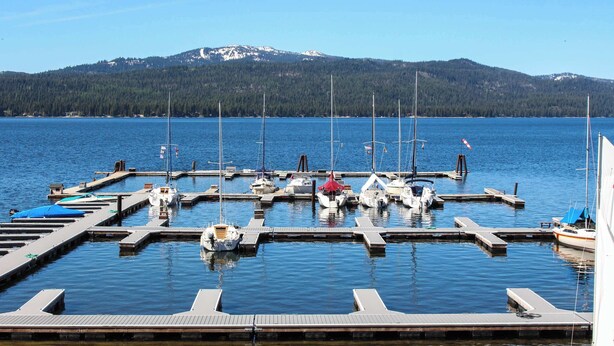 A marina with boats docked at wooden piers, surrounded by calm water and a forested mountain in the background. - 3BR Retreat | AC, Fireplace, Walk to Payette Lake (McCall)