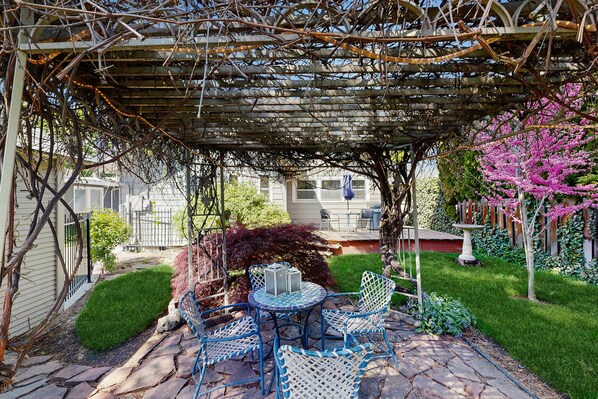 A covered patio with a table and chairs, surrounded by a garden with a pergola overhead. - Historic Craftsman Yard, Patio & Fireplace (Boise)