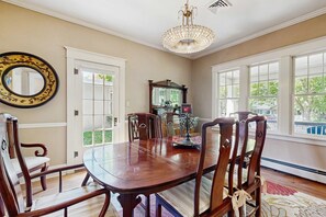 A dining room with a large wooden table, chairs, a chandelier, and large windows. - Historic Craftsman Yard, Patio & Fireplace (Boise)