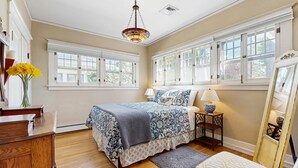 A bedroom with a large bed, two windows, a chandelier, a nightstand, and a dresser. - Historic Craftsman Yard, Patio & Fireplace (Boise)