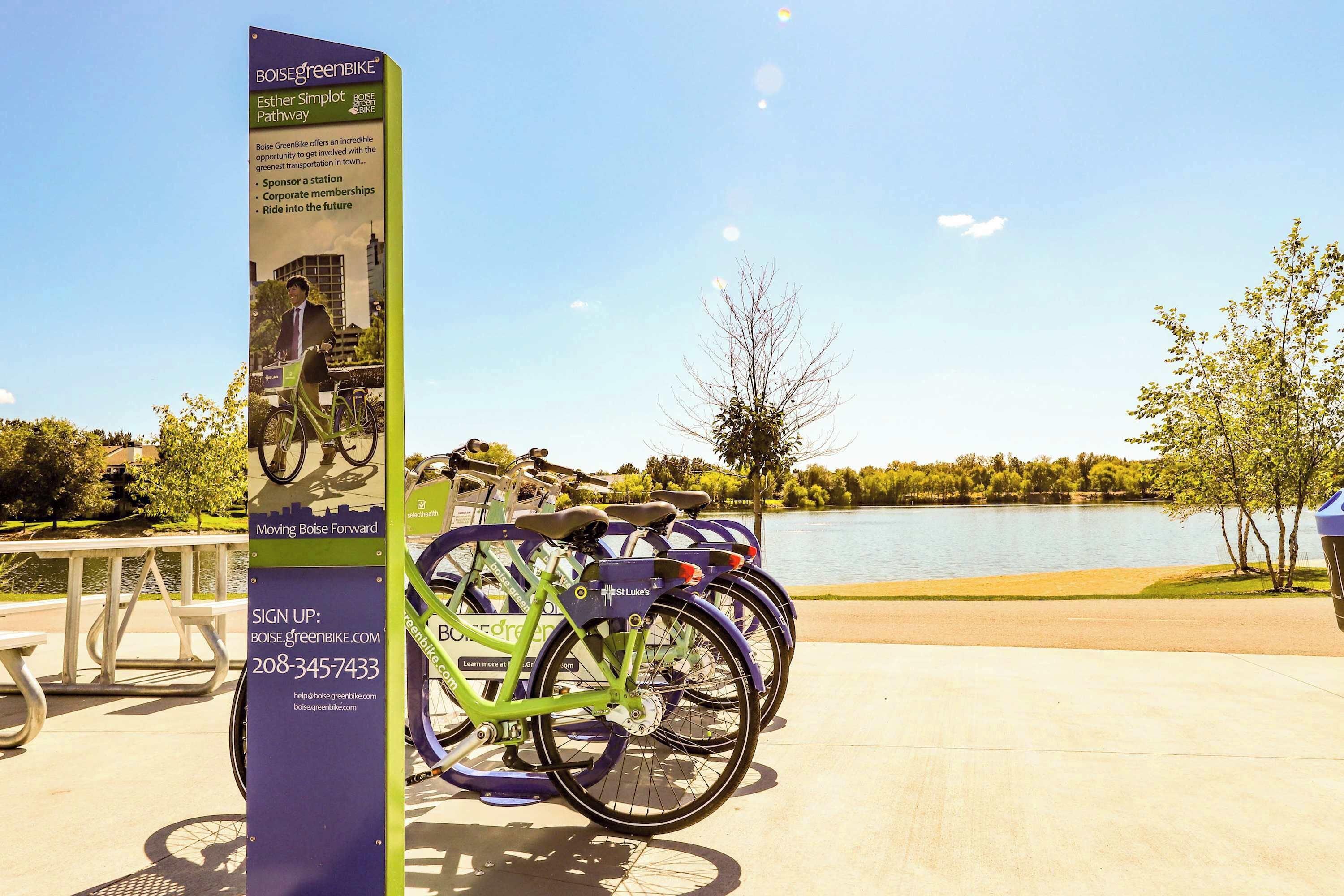 A green bicycle parked next to a signboard with contact information for Boise GreenBike.