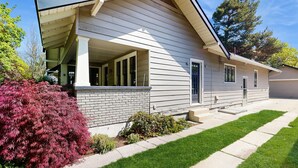 A single-story house with a covered porch, a brick foundation, and a well-maintained lawn. - Historic Craftsman Yard, Patio & Fireplace (Boise)