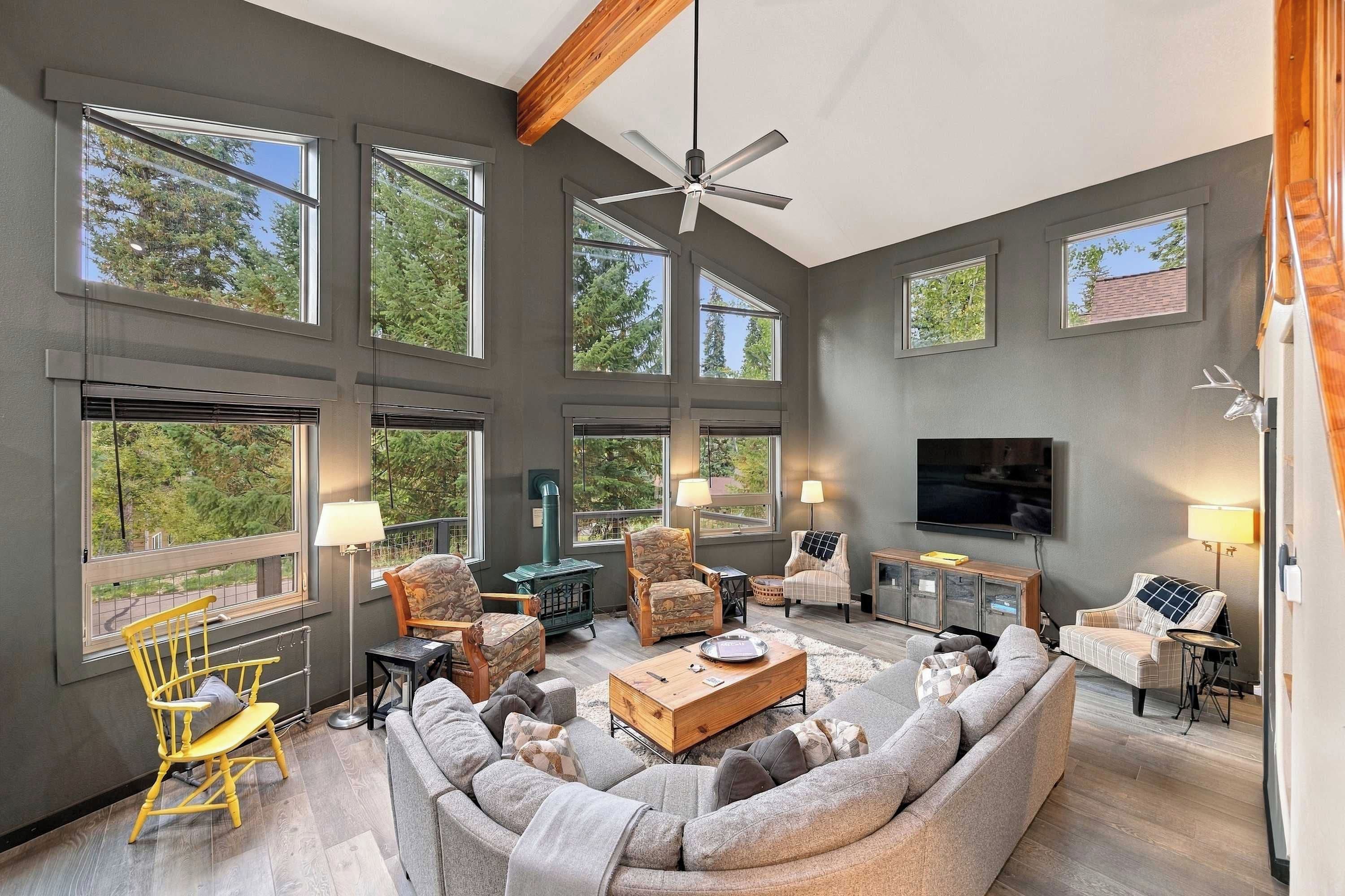 A spacious living room with large windows, a ceiling fan, and a television.
