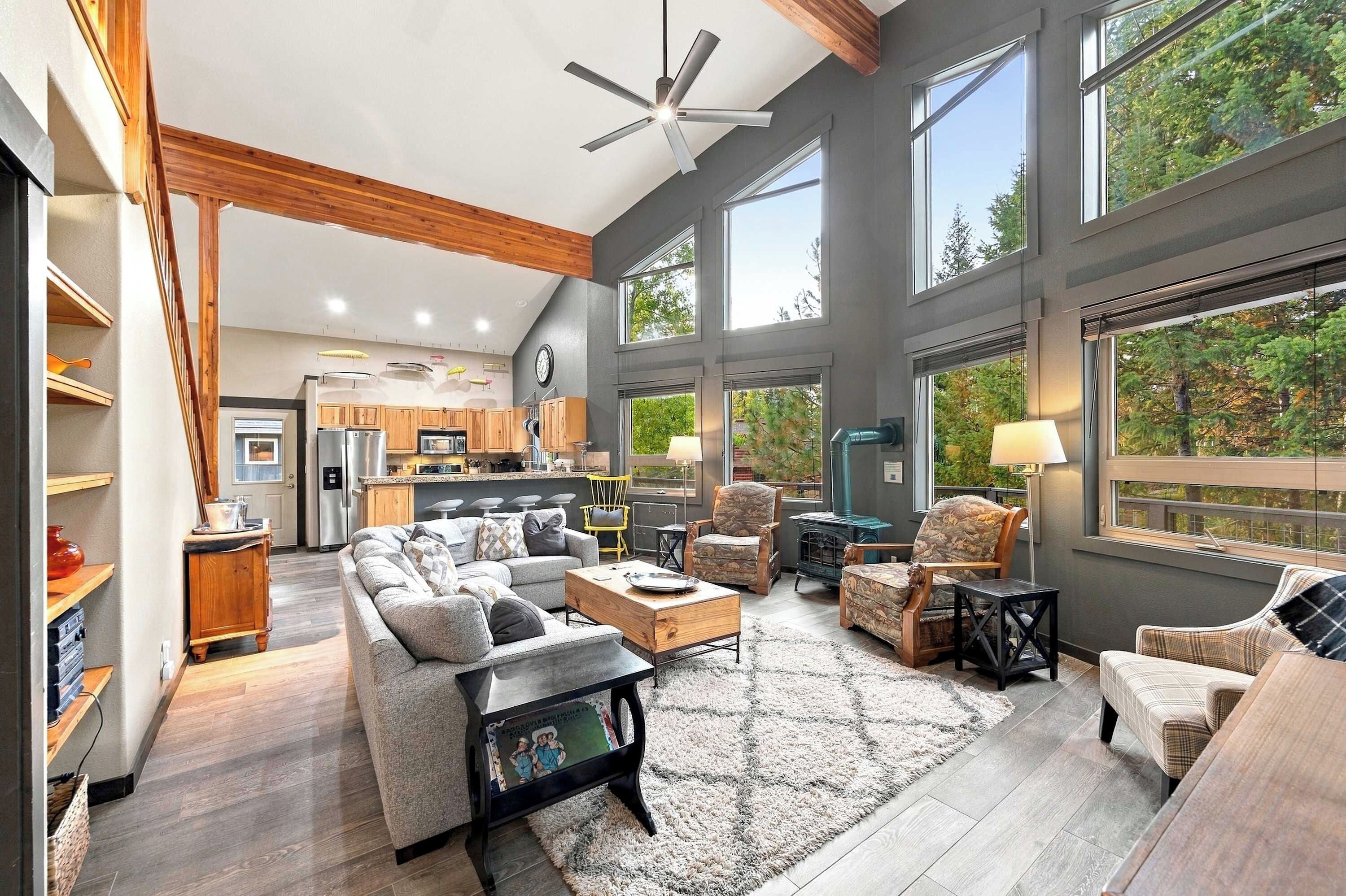 A spacious living room with a fireplace, large windows, and a modern kitchen in the background.