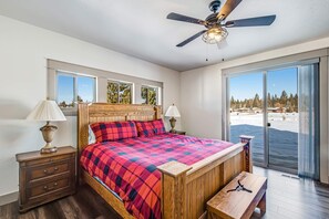 A bedroom with a wooden bed, two bedside tables with lamps, a ceiling fan, and a large sliding glass door leading to a balcony. - Luxury McCall Retreat | Hot Tub, Secret Bunk Room (McCall)