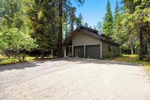 A two-story building with a garage, surrounded by tall trees.