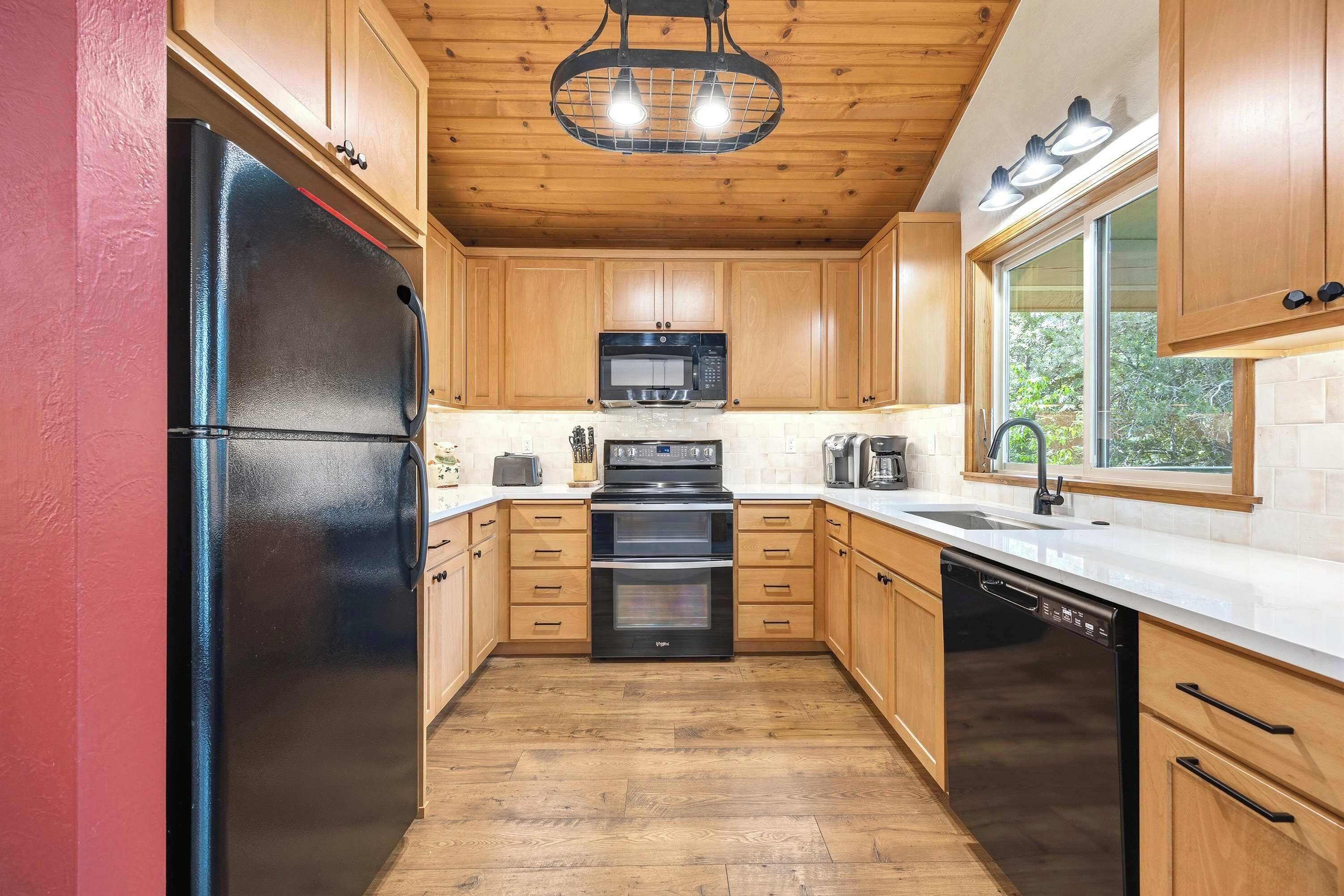 Una cocina con armarios de madera, un refrigerador negro, un microondas, un horno y un lavavajillas.