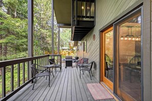 A wooden deck with outdoor furniture, a grill, and a glass door leading to the interior.
